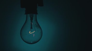 Karanlıkta mavi bir fonda ampul yanıyor. Tungsten ampulünü yavaşça aç. Yanıp sönen eski bir ampulün filamanı. Enerji, elektrik, ışık, yaşam. Yenilik kavramı.