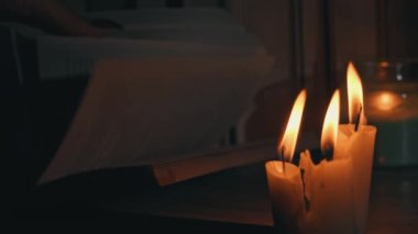 Kadınların elleri mum ışığında eski bir kitabı karıştırır. Sarı mumlarla dolu eski kütüphanenin atmosferi. Düşük ışıkta eski bir kitabın gece okuması. Geceleri kütüphane, eski edebiyat kitapları..