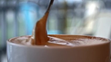 Kahve dükkanında bir fincan kahve tezgahının üzerinde duruyor ve kaşıkla karıştırılıyor. Masada köpüklü sıcak kapuçino var. Samimi bir kahve dükkanında randevum var..