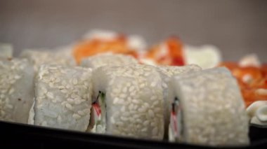 Sushi roll is spinning in a black container close-up. Japanese cuisine sushi in a restaurant. Sushi roll with salmon and vegetables. Japan restaurant menu. Side view.