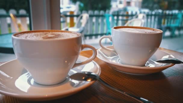 咖啡店的桌子上有两杯咖啡 热卡布奇诺与泡沫冷却在桌子上 在一家舒适的咖啡店约会 一对夫妇用白杯喝咖啡 — 图库视频影像