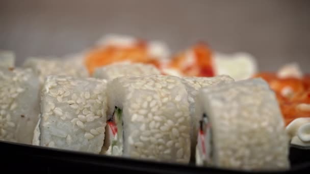 寿司ロールは黒の容器のクローズアップで回転しています レストランで和食寿司 寿司は鮭と野菜で転がす 日本のレストランメニュー サイドビュー — ストック動画