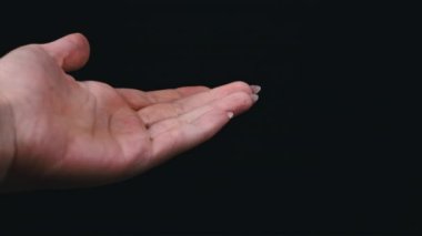 Kadın eline siyah arka plandaki bir kavanozdan beyaz haplar döküyor. Kız elinde tuttuğu kapsül dağını inceliyor. Evinde bir kadın duruyor, evinde ilaçlarla.