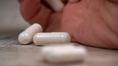 Woman pours white pills into her hand from a jar. The girl examines the mountain of capsules that she has in her hand. A woman stands in her house, apartment with medicine in her hand.