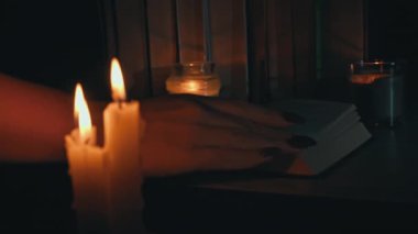 Kadınların elleri mum ışığında eski bir kitabı karıştırır. Sarı mumlarla dolu eski kütüphanenin atmosferi. Düşük ışıkta eski bir kitabın gece okuması. Geceleri kütüphane, eski edebiyat kitapları..