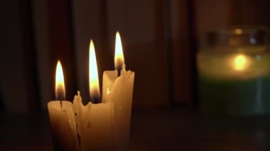 Candles burn in dark against background of a shelf with old books. Atmosphere of old library with yellow candles. Night reading of an old book in low light. Library at night, reading old literature.