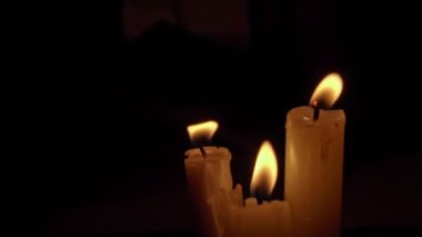 Siyah arka planda sarı renkli beyaz parafin mumlar. Bir mum hareketsiz yanar ve ateş yayar..