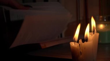 Kadınların elleri mum ışığında eski bir kitabı karıştırır. Sarı mumlarla dolu eski kütüphanenin atmosferi. Düşük ışıkta eski bir kitabın gece okuması. Geceleri kütüphane, eski edebiyat kitapları..