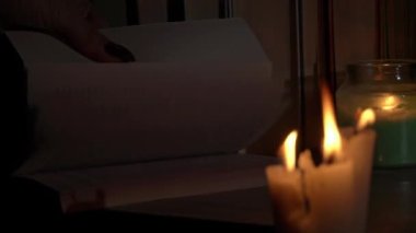Kadınların elleri mum ışığında eski bir kitabı karıştırır. Sarı mumlarla dolu eski kütüphanenin atmosferi. Düşük ışıkta eski bir kitabın gece okuması. Geceleri kütüphane, eski edebiyat kitapları..