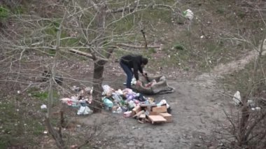 Evsiz biri çöpleri büyük bir çöp yığınının yanına yerleştirir. Evsiz bir adam bahçedeki çöpleri karıştırıyor. Çöpleri ayıklamak, şişeleri vermek..