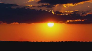 Parlak turuncu gün batımı bulutların arkasında batıyor. Günün sonunda, güneş ufkun altına batar. Ufkun yukarısındaki sıcak hava bükümünde büyük kırmızı güneş..