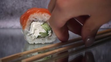 Suşi rulosu yemek çubuklarıyla yakından çekilir. Bir restoranda Japon mutfağı suşisi. Somon ve sebzeli suşi. Japon restoran menüsü. Yan görünüm.