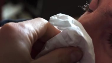 Kırmızı burunlu bir adam burnunu yakın plan beyaz bir peçeteye sildi. Hasta bir insan burnunun akmasından muzdarip. Viral enfeksiyon. Sağlık hizmetleri. Ev tedavisi.
