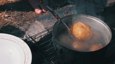 Patatesler gün boyunca açık bir ateşin üzerinde büyük bir kazanda pişirilir. Ormanda piknik. Tencere yanıyor ve su kaynıyor. Bir kamp tenceresi odun ateşinde yeni patatesler pişirir..