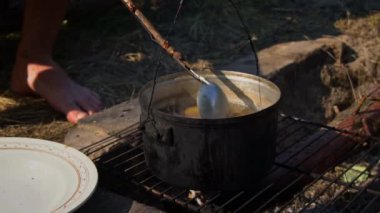 Patatesler gün boyunca açık bir ateşin üzerinde büyük bir kazanda pişirilir. Ormanda piknik. Tencere yanıyor ve su kaynıyor. Bir kamp tenceresi odun ateşinde yeni patatesler pişirir..