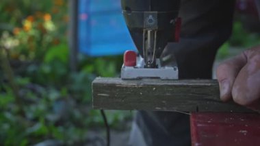 Adam tahtada yapbozla çalışıyor. Ellerinde elektrikli yapboz olan usta marangozun elleri odun kesiyor. Eller odun kesmek için yapboz kullanır. Atölyede yapbozla odun kesmek.