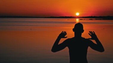 Gün batımında tek başına elini kaldırmış bir adamın siluetleri. Dalgın bir adam gün batımında suyun yanında oturur. Hayalci bir adamın silueti turuncu gökyüzüne büyük bir güneşle bakıyor..