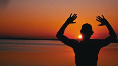 Gün batımında tek başına elini kaldırmış bir adamın siluetleri. Dalgın bir adam gün batımında suyun yanında oturur. Hayalci bir adamın silueti turuncu gökyüzüne büyük bir güneşle bakıyor..