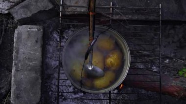 Patatesler gün boyunca açık bir ateşin üzerinde büyük bir kazanda pişirilir. Ormanda piknik. Tencere yanıyor ve su kaynıyor. Bir kamp tenceresi odun ateşinde yeni patatesler pişirir..