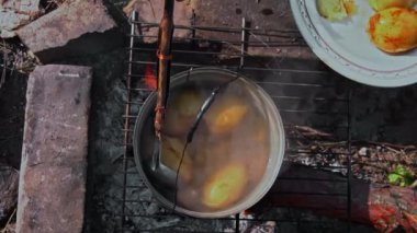 Patatesler gün boyunca açık bir ateşin üzerinde büyük bir kazanda pişirilir. Ormanda piknik. Tencere yanıyor ve su kaynıyor. Bir kamp tenceresi odun ateşinde yeni patatesler pişirir..