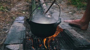 Patatesler gün boyunca açık bir ateşin üzerinde büyük bir kazanda pişirilir. Ormanda piknik. Tencere yanıyor ve su kaynıyor. Bir kamp tenceresi odun ateşinde yeni patatesler pişirir..