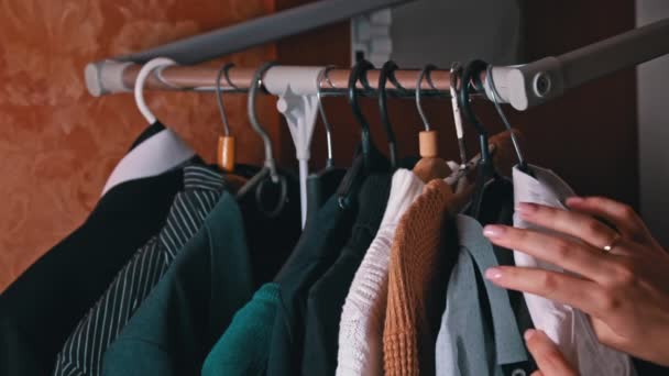 ウォーマンズはハンガーのクローズアップで物を選択する 女の子が店で手を差し伸べ 販売のためにハンガーに掛かる服を選ぶ ワードローブと選択の問題 — ストック動画