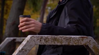 Erkek eller sonbahar atmosferinde yakın çekim bir bardak kahve alır. Genç bir adam parkta yürürken kahve içer. Yaşam tarzı. Sonbahar yürüyüşü konsepti.