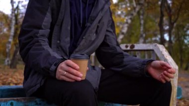 Erkek eller sonbahar atmosferinde yakın çekim bir bardak kahve alır. Genç bir adam parkta yürürken kahve içer. Yaşam tarzı. Sonbahar yürüyüşü konsepti.