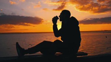 Gün batımında siluetli adam bankta kahve içiyor. Doğada akşam mis kokulu kahve. Bir adam gün batımında kahveyi sever. Doğayla baş başa düşünceler. Serbest düşünce konsepti.