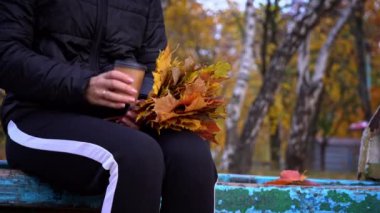 Bir kadın sonbahar atmosferinde yakın plan bir fincandan kahve içer. Genç bir kız parkta yürürken kahve içer. Yaşam tarzı. Sonbahar yürüyüşü konsepti.