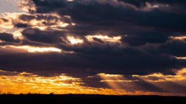 Kalkan bulutların arkasında parlak turuncu gün batımı. Güneş, günün sonunda ufkun altına iniyor. Parlayan güneşle gün batımı bulutların arasından iniyor zaman akıp gidiyor..