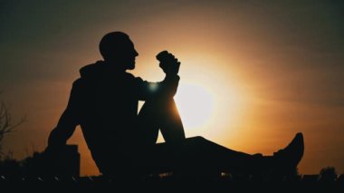 Gün batımında siluetli adam bankta kahve içiyor. Doğada akşam mis kokulu kahve. Bir adam gün batımında kahveyi sever. Doğayla baş başa düşünceler. Serbest düşünce konsepti.