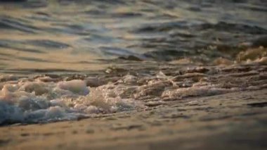 Dalgalar kıyıda günbatımını yavaş çekimde yansıtıyor. Güneşli bir yaz gününde suda dalgalanmalar. Güneş ışınlarının suya yansıması. Batan güneş görkemli dalgalara yansıyor..