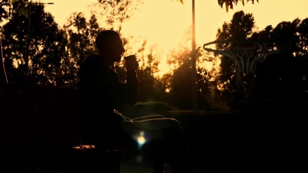 Silhouetted Man Bij Zonsondergang Drinkt Koffie Een Bank Geurende Koffie — Stockvideo