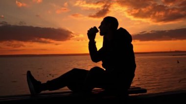 Gün batımında siluetli adam bankta kahve içiyor. Doğada akşam mis kokulu kahve. Bir adam gün batımında kahveyi sever. Doğayla baş başa düşünceler. Serbest düşünce konsepti.