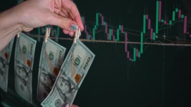 Dolar, kripto para birimi grafiğinin arka planında bir mandalda asılı duruyor. Borsa ve borsa fiyat verileri borsa duvarında. Mali endeksler zamanla yükselip alçalıyor.