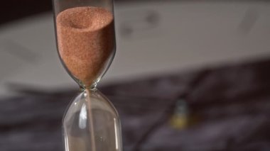 Kum saati arka plandaki sıradan mekanik saate doluyor. Kum yağıyor ve zamanı sayıyor. Zaman akıp gidiyor, zamanın geçişi. Geri sayım, dakika, saniye, saat.