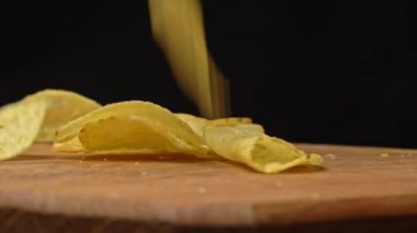 Patates cipsleri ağır çekimde ahşap bir tabağa düşer. Abur cubur. Sağlıksız fast food için patates çerezi. Sağlıksız yaşam tarzı ve hızlı karbonhidratlar..