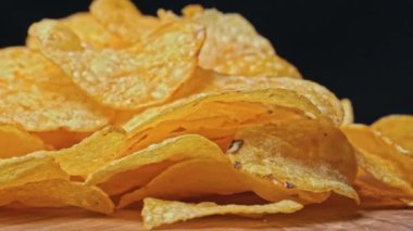 Patates cipsi kıvrılıp duruyor. Sağlıksız fast food için patates çerezi. Siyah arka planda kaotik bir şekilde saçılmış çipler. Abur cubur, fast food. Kızarmış patatesler yakın..