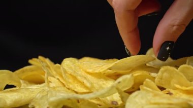 Adam elleriyle çıtır patates cipsi alıyor. Sağlıksız fast food için patates çerezi. Siyah arka planda kaotik bir şekilde saçılmış çipler. Abur cubur, fast food. Kızarmış patatesler yakın..