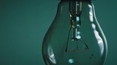 Light bulb flashes on a blue background in the dark. Slow turning on and off of a tungsten light bulb. Filament of a blinking vintage light bulb. Energy, electricity, light, life.