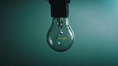 Light bulb flashes on a blue background in the dark. Slow turning on and off of a tungsten light bulb. Filament of a blinking vintage light bulb. Energy, electricity, light, life.