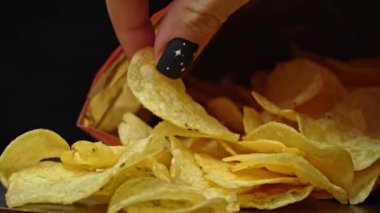 Adam elleriyle çıtır patates cipsi alıyor. Sağlıksız fast food için patates çerezi. Siyah arka planda kaotik bir şekilde saçılmış çipler. Abur cubur, fast food. Kızarmış patatesler yakın..