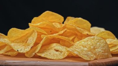 Patates cipsi kıvrılıp duruyor. Sağlıksız fast food için patates çerezi. Siyah arka planda kaotik bir şekilde saçılmış çipler. Abur cubur, fast food. Kızarmış patatesler yakın..