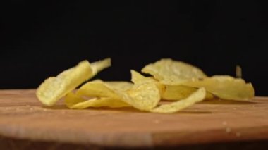 Patates cipsleri ağır çekimde ahşap bir tabağa düşer. Abur cubur. Sağlıksız fast food için patates çerezi. Sağlıksız yaşam tarzı ve hızlı karbonhidratlar..