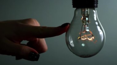 Light bulb turns on and goes out at the touch of a persons hand in the dark. Slow turning on and off of a tungsten light bulb. Filament of a blinking vintage light bulb. Energy, electricity, light