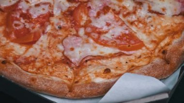 Salamlı ve pastırmalı bir pizza, siyah arka planda bir kutuda dönüyor. Et ve peynirli taze pizza iştah açıcı. Yanları hazır İtalyan pizzası. Fast food.