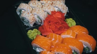 Sushi roll is spinning in a black container close-up. Japanese cuisine sushi in a restaurant. Sushi roll with salmon and vegetables. Japan restaurant menu. Side view.