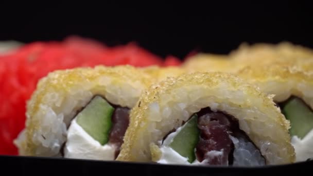 寿司ロールは黒の容器のクローズアップで回転しています レストランで和食寿司 寿司は鮭と野菜で転がす 日本のレストランメニュー サイドビュー — ストック動画