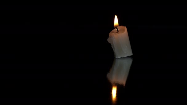 短いパラフィンキャンドルが黒い背景に反射して燃える 1つのライトキャンドルは暗い背景に対して明るいオレンジ色の炎で燃えます 悲しみの象徴 死者の記憶 戦争の概念 — ストック動画